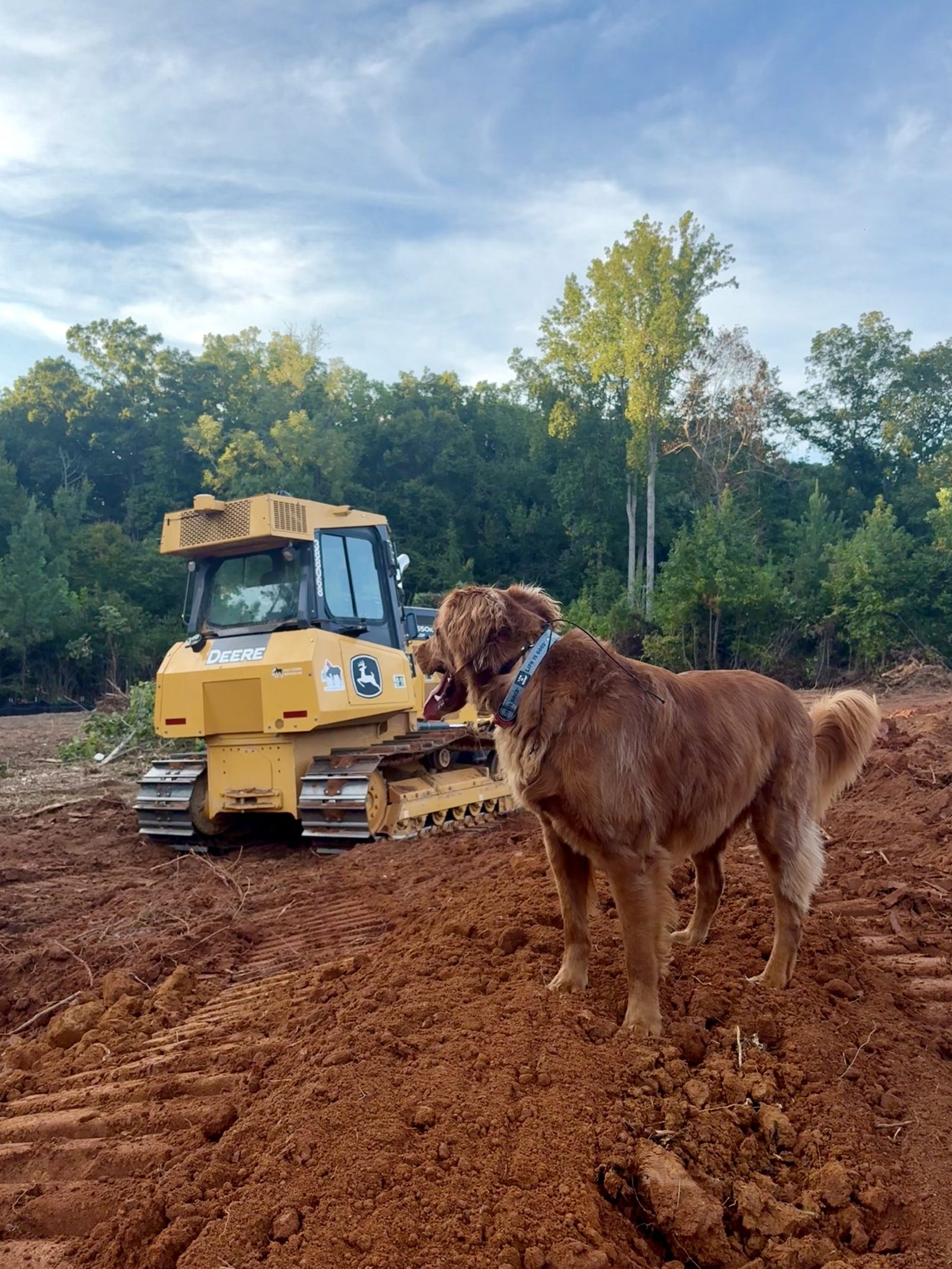 Scooter facing a John Deere dozer on cleared red dirt